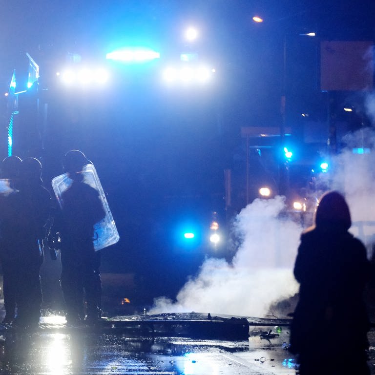 Polizisten stehen bei Zusammenstößen zwischen Randalierern und der Polizei mit Schilden auf einer Kreuzung.