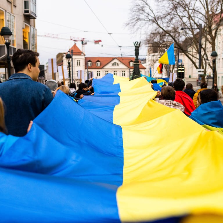 Menschen geehen während eines Marsches gegen den Angriffskrieg Russlands gegen die Ukraine durch die Innenstadt von Freiburg und halten dabei ein Banner in den ukrainischen Nationalfarben.  (Foto: dpa Bildfunk, picture alliance/dpa | Philipp von Ditfurth)