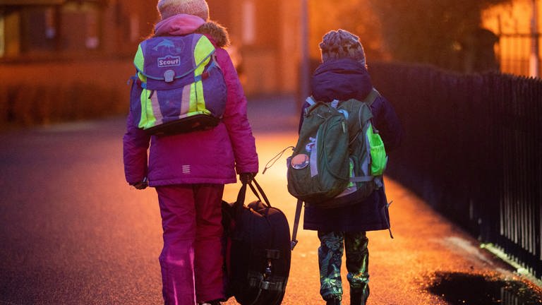 Zwei Schüler gehen am frühen Morgen auf dem Schulweg zu ihrer Schule (Symbolbild)