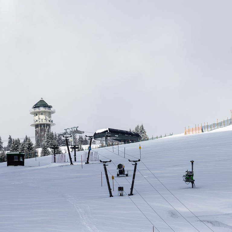 Schnee liegt auf einer Skispiste unter den Masten eines stillstehenden Lifts, während im Hintergrund der Feldbergturm zu sehen ist. (Foto: dpa Bildfunk, picture alliance/dpa | Philipp von Ditfurth)