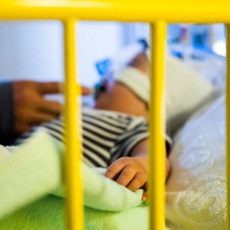Ein Vater streichelt seinen achteinhalb Monate alten Sohn, der mit einem Atemwegsinfekt auf der Intensivstation einer Kinderklinik liegt und non-invasiv beatmet wird (Archivbild).  (Foto: dpa Bildfunk, picture alliance/dpa | Christoph Soeder)