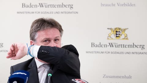 Manfred Lucha (Grüne), Sozialminister in Baden-Württemberg, demonstriert bei einer Pressekonferenz zum Thema Coronavirus das korrekte Niesen in eine Armbeuge. 