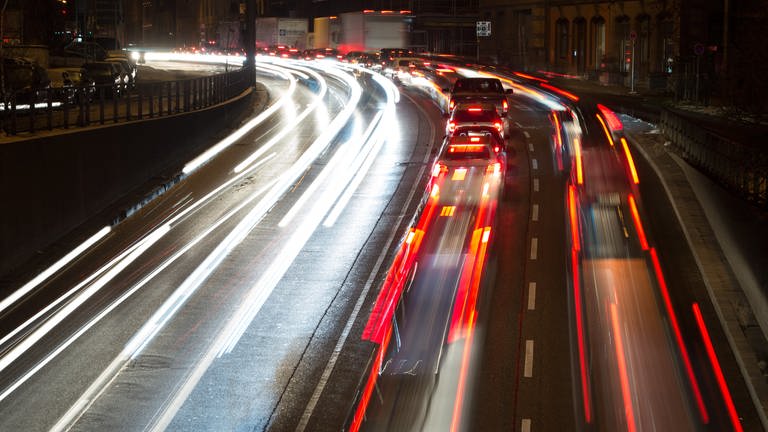 Autos fahren nachts auf einer Straße, die Lichter verschwimmen durch einen Zeitraffer-Effekt.