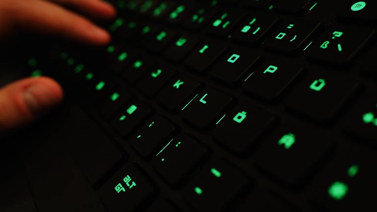 Ein Mann tippt auf einer beleuchteten Tastatur an einem Laptop. Symbolbild zu Hackerangriff auf IT-Dienstleister für Krankenkassen. (Foto: dpa Bildfunk, picture alliance/dpa | Nicolas Armer)