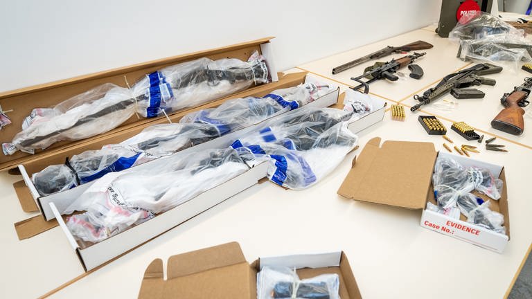 Beweismittel in Form von Waffen, die bei einem SEK-Einsatz in Boxberg (Main-Tauber-Kreis) sichergestellt wurden, liegen eingepackt in Plastikfolie auf einem Tisch im Polizeipräsidium Heilbronn. Zur Veranschaulichung liegen daneben typgleiche Waffen. 