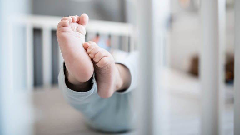 Die Füße eines Babys sind in einem Kinderbett zu sehen. 