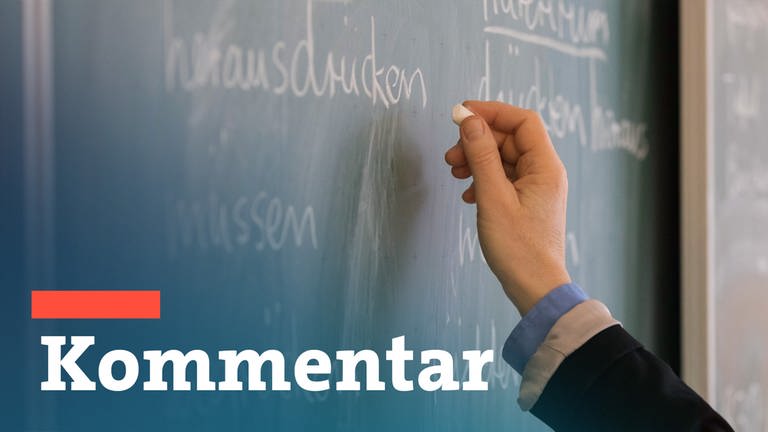 Eine Lehrerin steht in einem Klassenraum an einer Tafel und schreibt. Im Vordergrund steht: Kommentar.
