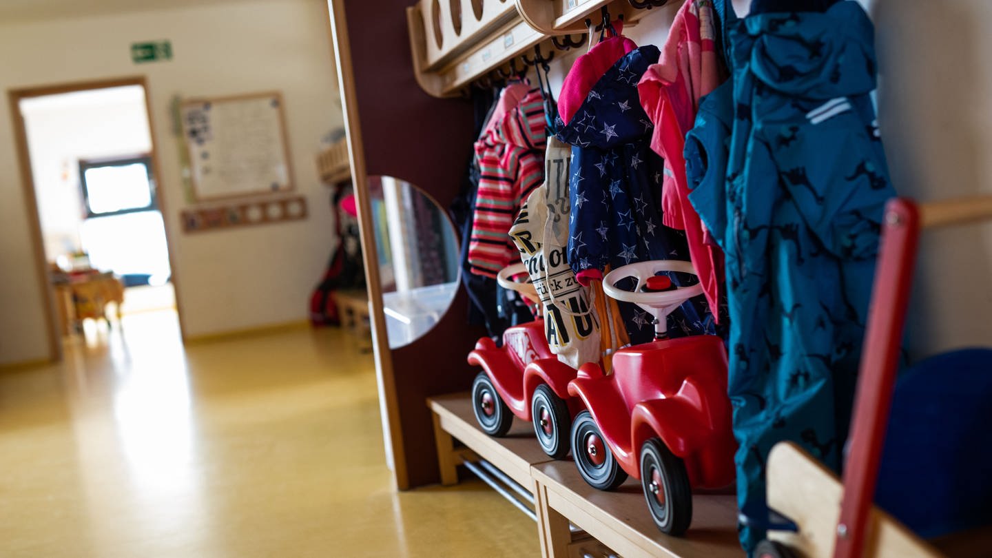 Bobbycars stehen unter Jacken von Kindern, die an einer Garderobe einer Kindertagesstätte (Kita) hängen. (Foto: picture-alliance / Reportdienste, picture alliance/dpa | Philipp von Ditfurth)