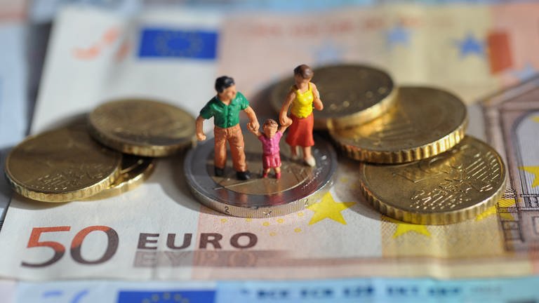 Ein Figuren-Paar mit einem Kind steht auf einer Zwei-Euro-Münze, die auf einem 50-Euro-Schein liegt. (Foto: dpa Bildfunk, picture alliance / dpa | Andreas Gebert)