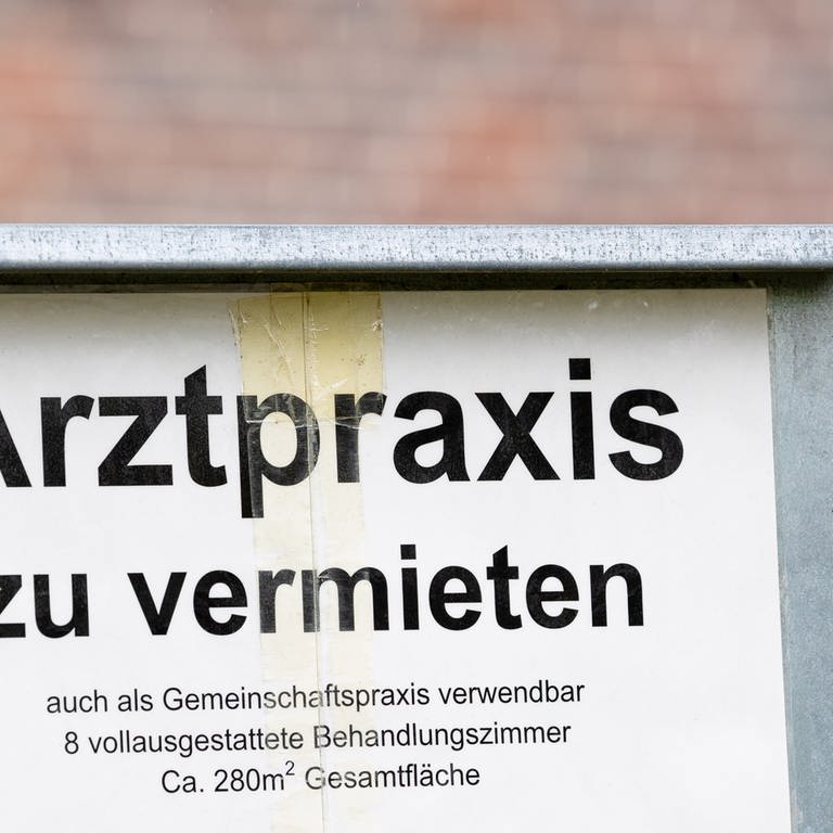 Ein Schild mit der Aufschrift "Arztpraxis zu vermieten" steht vor einem Gebäude.