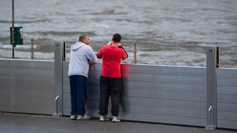 Zwei Schaulustige stehen an den Spundwänden, zum Schutz gegen das Hochwasser aufgebaut wurden.  (Foto: dpa Bildfunk, Picture Alliance)