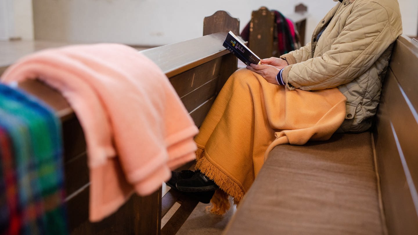 Eine Frau sitzt mit einer Decke in der Kirche. Auch Kirchen müssen wegen der Energiekrise unter anderem beim Heizen sparen. (Foto: picture-alliance / Reportdienste, Picture Alliance)