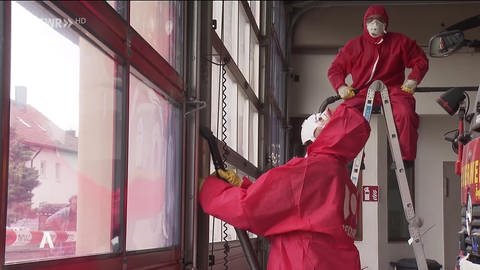 Männer in roten Overalls und mit Atemmasken reinigen das Feuerwehrgerätehaus (Foto: SWR)