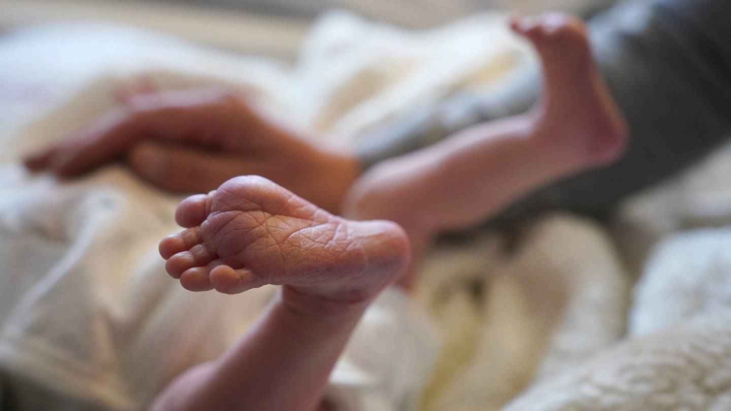 Säugling liegt zwischen seinen Eltern auf dem Bett in einer Geburtshilfestation (Foto: dpa Bildfunk, picture alliance/dpa | Marcus Brandt)