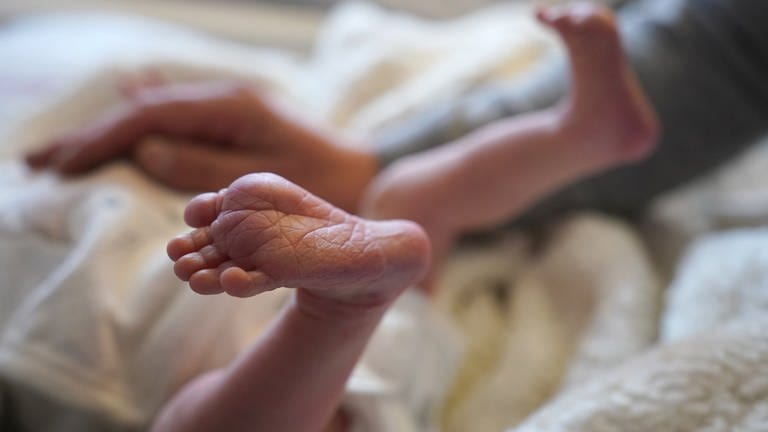 Säugling liegt zwischen seinen Eltern auf dem Bett in einer Geburtshilfestation