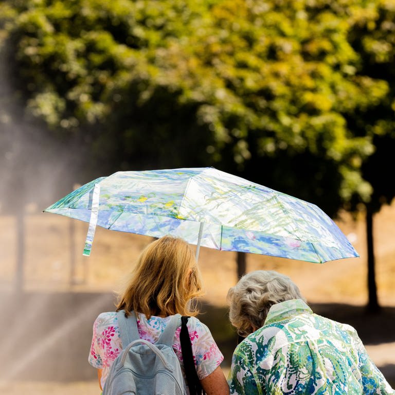 Zwei Frauen schützen sich am Rheinufer in der Kölner Altstadt mit einem Regenschirm vor der Sonne.