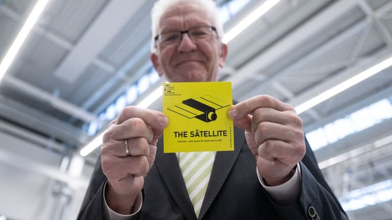 Winfried Kretschmann (Bündnis 90Die Grünen), Ministerpräsident von Baden-Württemberg, zeigt während eines Besuchs der Universität Stuttgart einen Aufkleber mit der Aufschrift „The Sätellite“.