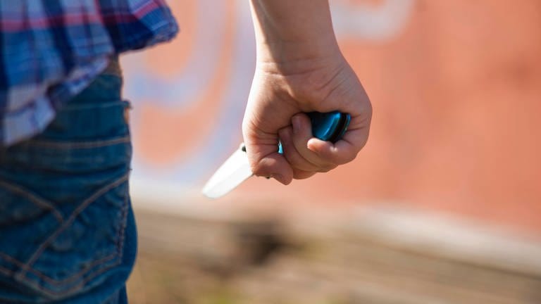 Ein junger Mensch steht mit einem Messer in der Hand vor einer Graffitiwand. (Foto: dpa Bildfunk, Symbolbild | picture alliance / imageBROKER | uwe umstätter)