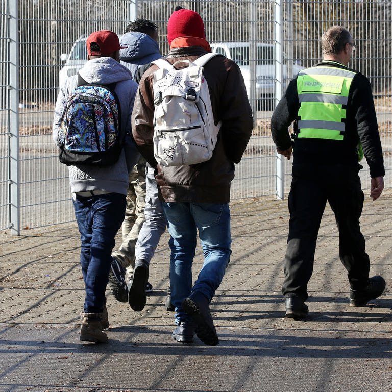 Mitarbeiter einer Sicherheitsfirma begleiten auf dem Gelände der Erstaufnahmestelle in Sigmaringen eine Gruppe von Asylbewerbern (Archivbild). (Foto: dpa Bildfunk, picture alliance / Thomas Warnack/dpa | Thomas Warnack)
