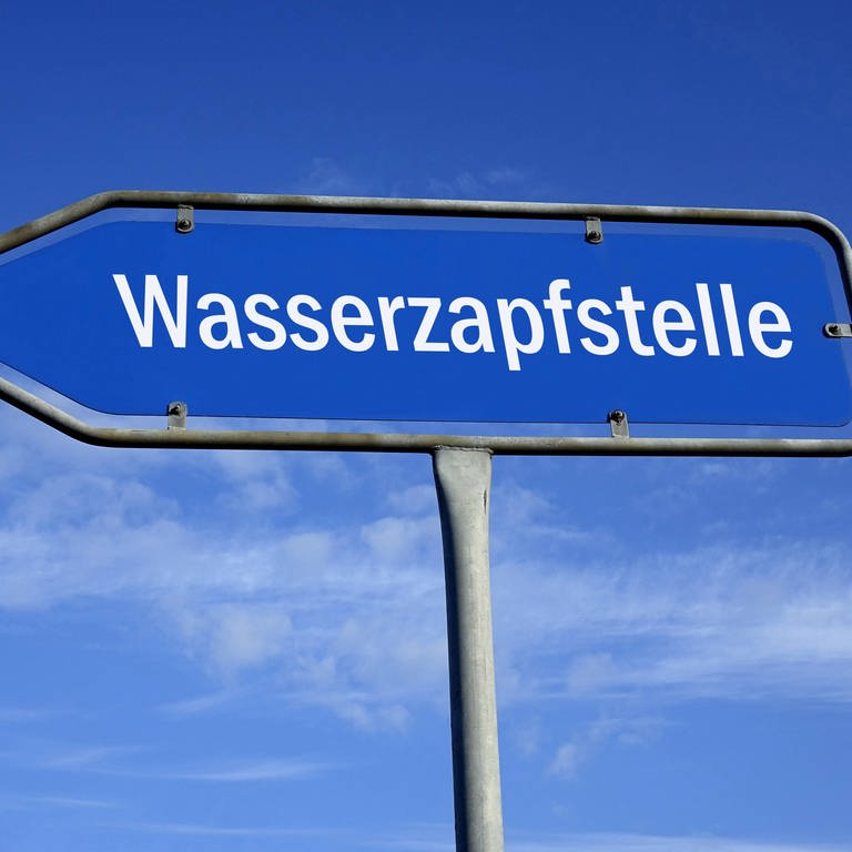 Ein blaues Wegweiser-Schild zeigt zu einer Wasserzapfstelle.  (Foto: IMAGO, IMAGO / Steinach, Symbol)