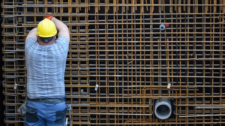 Ein Bauarbeiter beschäftigt sich auf einer Baustelle mit einer Stahlbetonwand. 