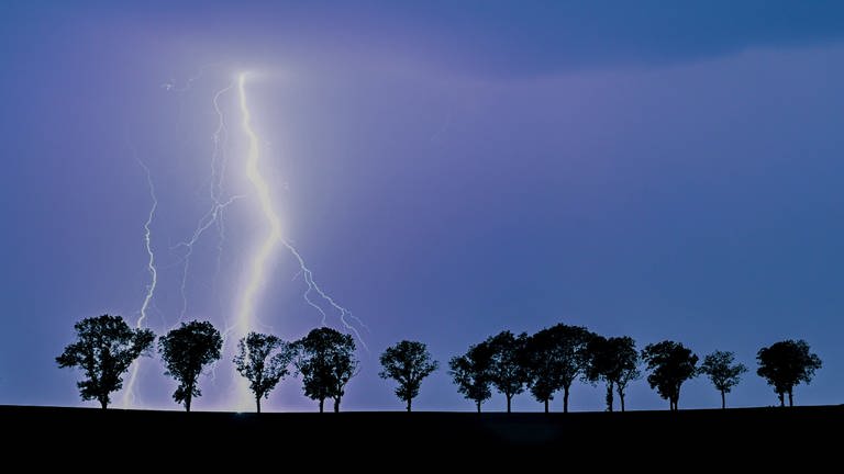 Ein Blitz eines Gewitters erhellt den Nachthimmel über der Landschaft.