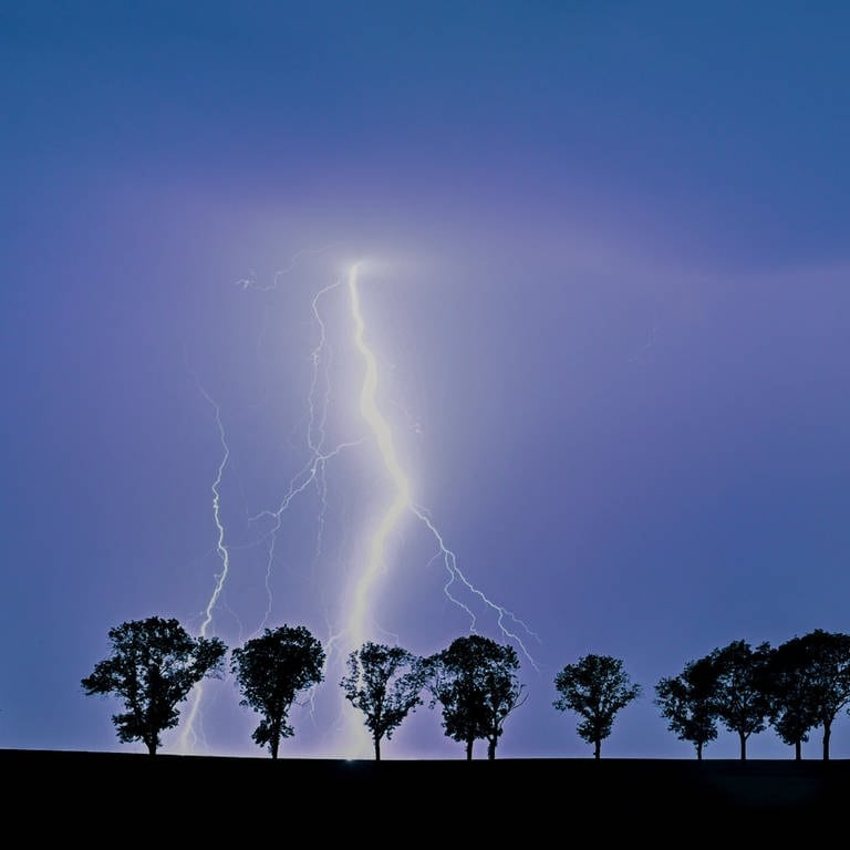Ein Blitz eines Gewitters erhellt den Nachthimmel über der Landschaft.