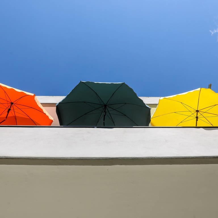 Drei Sonnenschirme stehen auf einem Balkon an einem Mehrfamilienhaus. (Foto: picture-alliance / Reportdienste, picture alliance/dpa | Thomas Warnack)