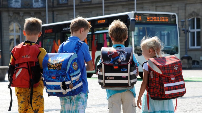 Kinder gehen auf einen Schulbus zu. 