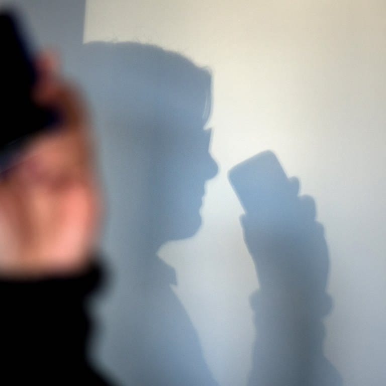 Eine Frau telefoniert mit ihrem Mobiltelefon - an der Wand zeichnet sich ihr Schatten ab. 