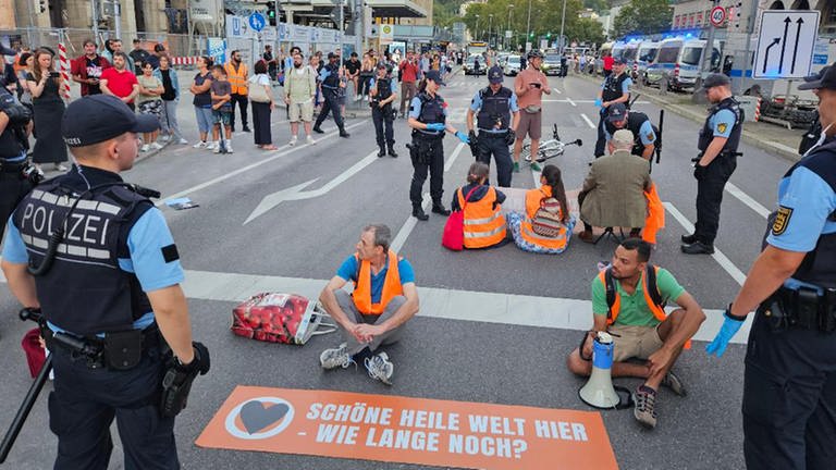 Aktivisten der Gruppe Letzte Generation sitzen bei einer Blockade auf der Straße vor dem Hauptbahnhof.