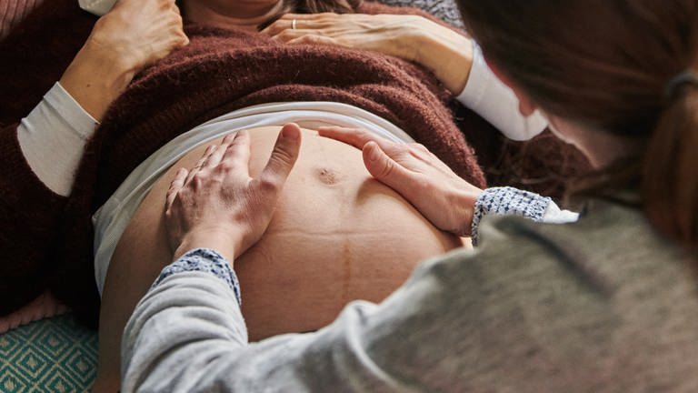 Eine Hebamme tastet in ihrer Praxis den Bauch einer schwangeren Frau ab. 
