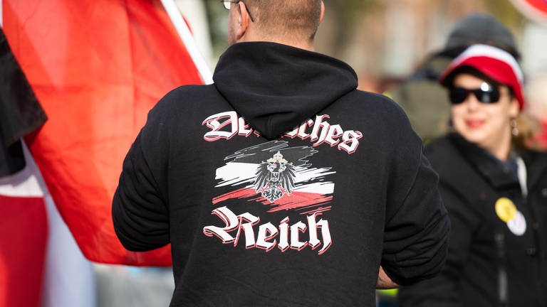 Ein Mann trägt einen Pullover mit dem Aufdruck „"Deutsches Reich" bei einer Demonstration von Reichsbürgern (Symbolbild).
