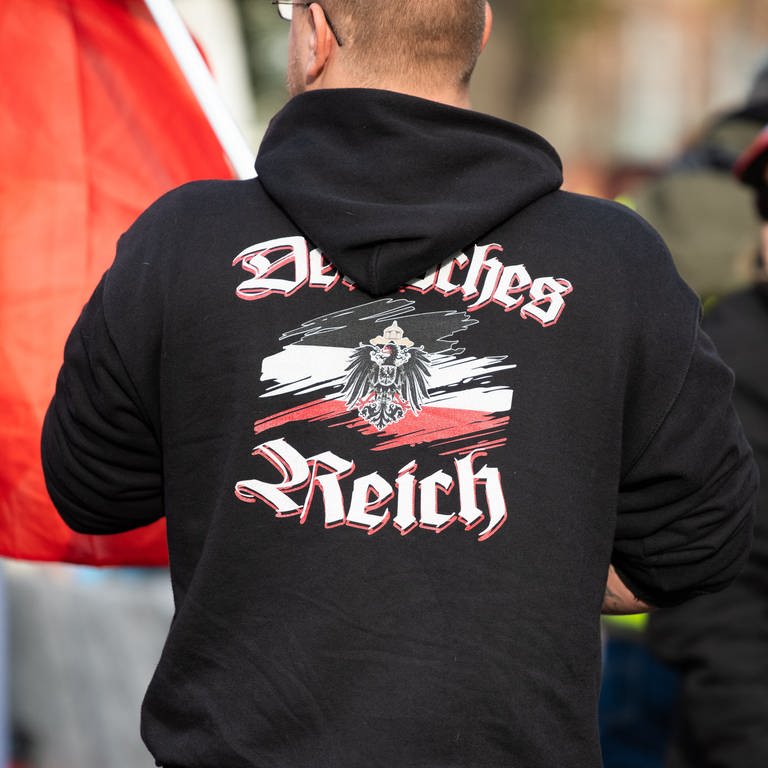 Ein Mann trägt einen Pullover mit dem Aufdruck „"Deutsches Reich" bei einer Demonstration von Reichsbürgern (Symbolbild).