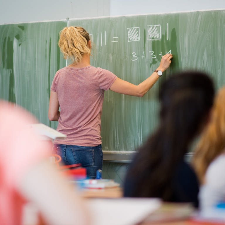Eine junge Lehrerin schreibt im Mathematikunterricht an eine Schultafel. 