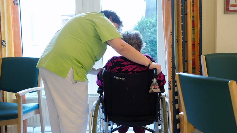 Pflegerin beugt sich über Frau in Rollstuhl