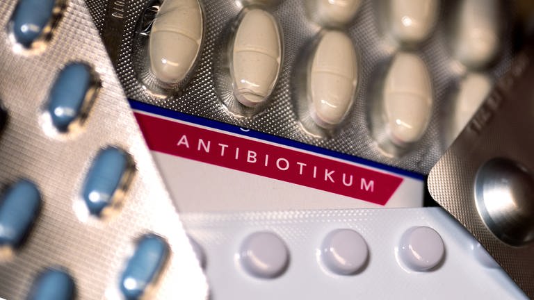 Eine Packung Antibiotika und diverse andere Medikamente liegen auf einem Tisch.