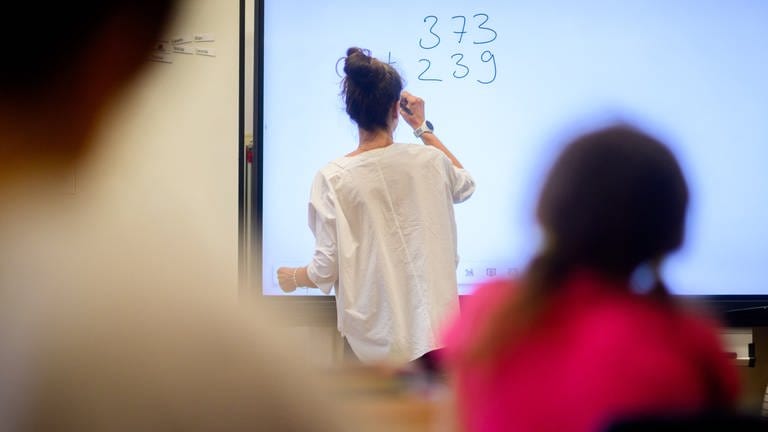 Ein Lehrerin schreibt eine Mathematikaufgabe auf eine digitale Schultafel im Klassenraum einer 4. Klasse einer Grundschule.  (Foto: dpa Bildfunk, picture alliance/dpa | Julian Stratenschulte)