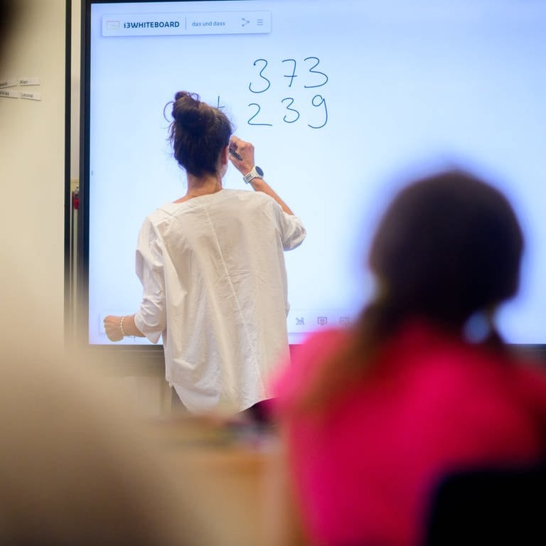 Ein Lehrerin schreibt eine Mathematikaufgabe auf eine digitale Schultafel im Klassenraum einer 4. Klasse einer Grundschule.  (Foto: dpa Bildfunk, picture alliance/dpa | Julian Stratenschulte)