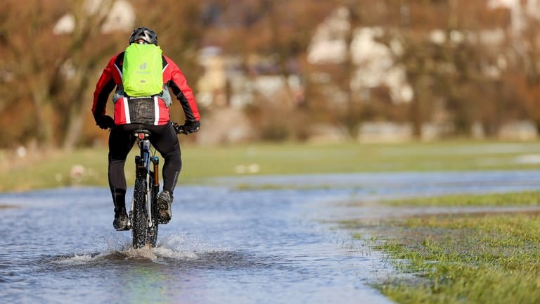 Ein Radfahrer ist auf dem überflutetem Donau Radwanderweg unterwegs. Milde Temperaturen und Regenfälle sorgen in den kommenden Tagen für steigende Pegelstände.
