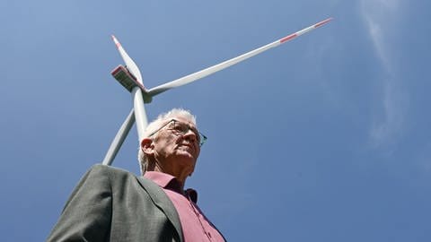 Archivbild: Winfried Kretschmann (Grüne) steht bei einer Besichtigung einer Baustelle einer Windkraftanlage vor einem schon gebauten Windrad. (Mai 2023)