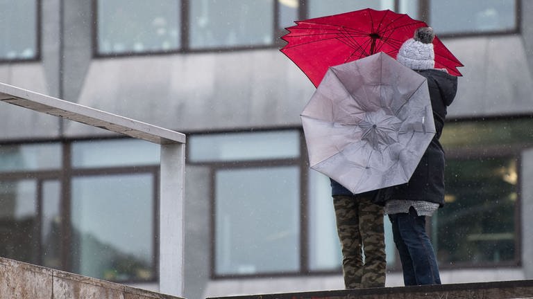 Zwei Passanten hantieren mit ihren Regenschirmen im Wind (Archivbild). (Foto: dpa Bildfunk, picture alliance/dpa | Marijan Murat (Archivbild))