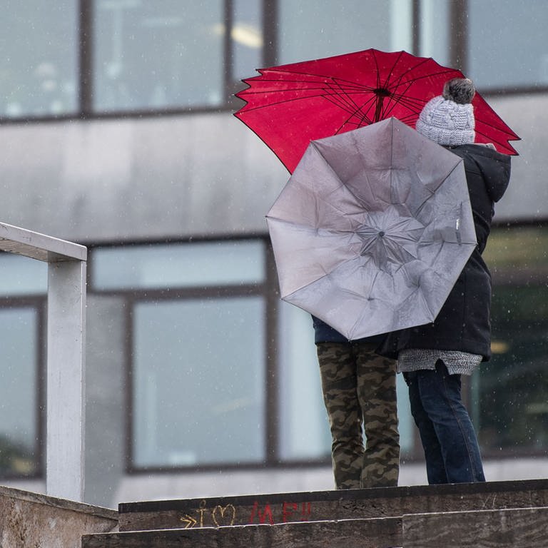 Zwei Passanten hantieren mit ihren Regenschirmen im Wind (Archivbild).