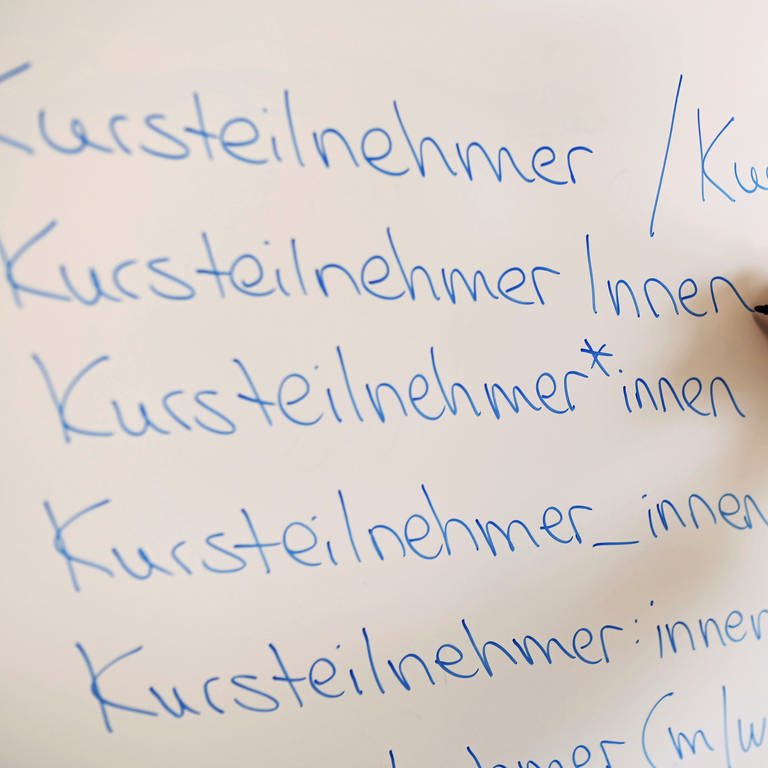 An einem Whiteboard steht das Wort Kursteilnehmer in verschiedenen Gender-Schreibweisen.