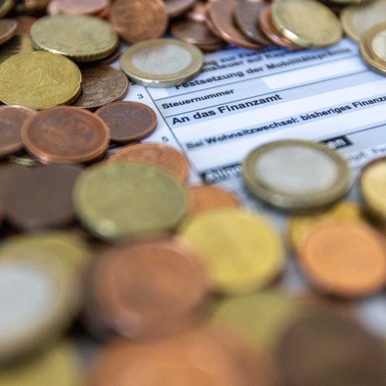 Ein Formular zur Steuererklärung ist von Euro-Münzen bedeckt. Baden-Württemberg muss in den kommenden Jahren mit weniger Steuereinnahmen auskommen, als ursprünglich geplant. 