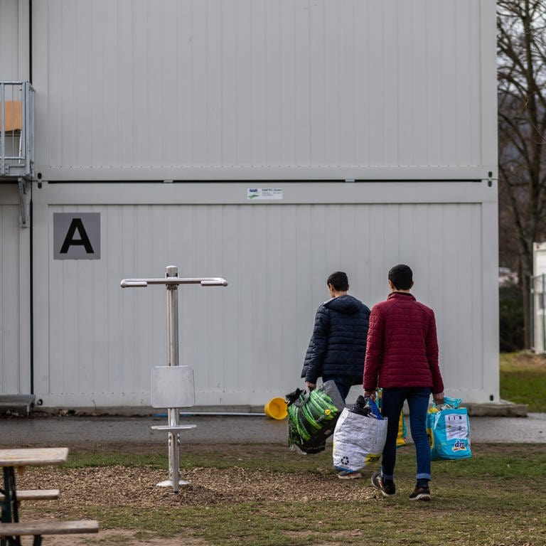 Zwei Bewohner der Landeserstaufnahmeeinrichtung (LEA) gehen mit Plastiktüten über das Gelände der Einrichtung in Freiburg. In Baden-Württemberg gibt es Kritik an der angeblich mangelnden Unterstützung des Bundes bei der Bereitstellung von Liegenschaften.