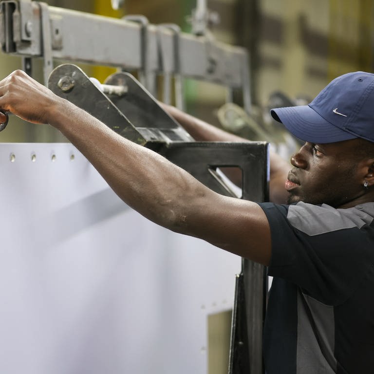 Ein Mann aus Gambia steht an einer Maschine in einem Unternehmen und arbeitet. 