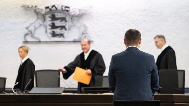 Anton Baron (vorne), Fraktionsvorsitzender der AfD im Landtag von Baden-Württemberg, steht vor einer Urteilsverkündung des Verfassungsgerichtshofs Baden-Württemberg in einem Gerichtssaal.