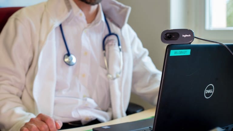 Symbolbild: Ein Hausarzt sitzt während einer Sprechstunde in seiner Praxis vor einem Laptop. Eine Cloudplattform soll allen Ärztinnen und Ärzten sowie Krankenhäusern zentralen Zugriff auf Patientendaten geben.