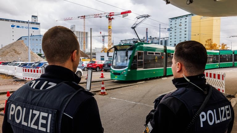 Eine Straßenbahn fährt auf den Grenzübergang in Weil am Rhein-Friedlingen zu während im Vordergrund zwei Beamte der Bundespolizei zu sehen sind. (Archivbild)